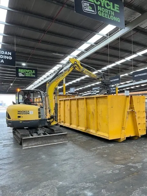 An excavator loading a hook bin inside the hall